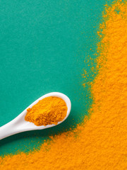 Turmeric Powder or Curcuma longa and white spoon with turmeric powder on green background. Top...