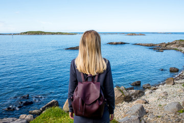 Women with backpack looks at the blue ocean in Norway. Enjoys scenic view landscape. Beautiful nature. Harmony, relax lifestyle. Travel, adventure. Sense of freedom. Explore North Norway. Scandinavia