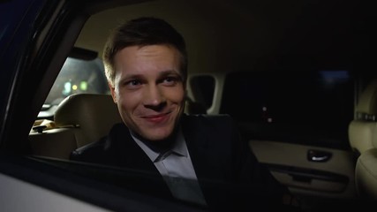 Handsome actor looking at public from car backseat, enjoying movie premier party