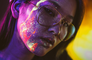 Beautiful young woman dancing and making party with fluorescent painting on her face. Neon facial portraits - obrazy, fototapety, plakaty