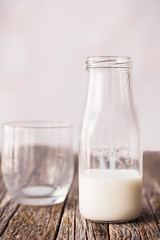 Semi-empty bottle of milk, next to empty glass, on rustic wooden table