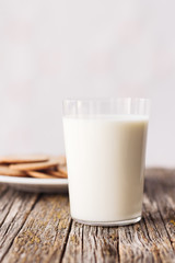 Glass of milk, next to plate of cookies, on rustic wooden table