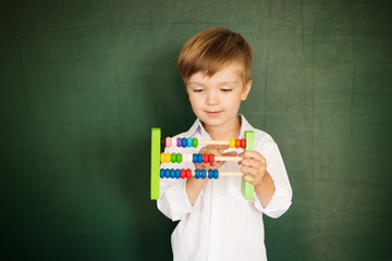 Little cute school boy is counting with bills in his hands against the background of the school board.