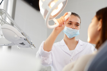 Low angle portrait of young female dentist adjusting lamp while examining patient in clinic, copy...
