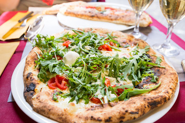 Italian pizza with arugula, tomato and cheese on the table in a restaurant outside over blurred background