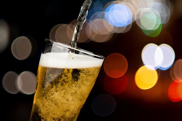 Beer pouring from bottle into glass on bokeh light night background drinking alcohol celebration concept design