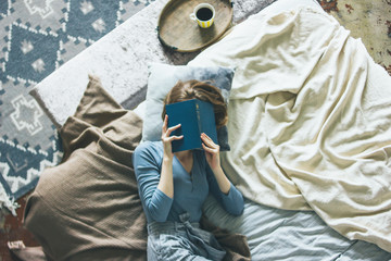 Young woman reading book on bed in loft room, slow life