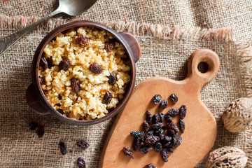 Sweet millet porridge with dark raisins in ceramic rustic bowl with walnuts in background