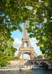 Fototapeta na wymiar Eiffel Tower through foliage of a lush tree - River Seine with Tourist Boat and Bridge 