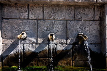 Three stone taps from which water flows. The water is clean and clear to drink. Cranes are made in the wall of an old building.