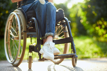young disabled girl in overall and white trainers sitting with crossed legs on the wheelchair. close up cropped photo.
