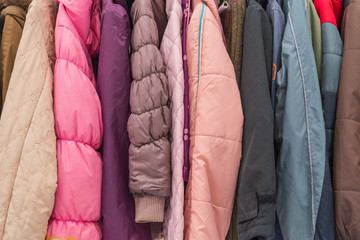 Row of colourful tone of adult winter jackets hang on aluminium hanger clothes rack in retail fashion store or second hand outlet shop.