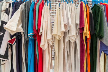 Row of colourful tone and white of T-shirts hang on aluminium hanger clothes rack in retail fashion store or second hand outlet shop.