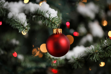 Traditional artificial Christmas tree with red ball ornament with glowing lights and snow in background - Powered by Adobe