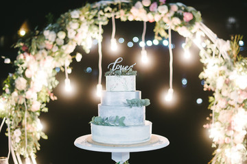 Decorated by flowers multilevel wedding cake with lights on the background