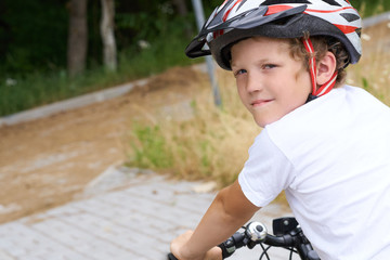 Back view of small boy in protective helmet riding bicycle in park on summer day. Weekend activity.