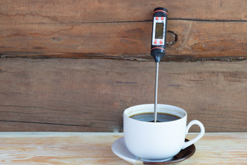 black coffee on a wooden background with a thermometer