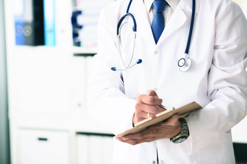Male doctor in white coat on duty writes information with pen in clipboard closeup. Selective focus. Health and medical concept.