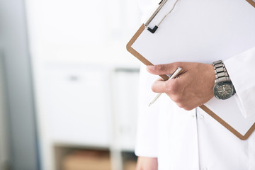 Close-up of clipboard with blank paper in medical doctor hand. Young male therapist is preparing for an interview with a patient.