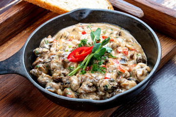 Fried snails in cream sauce, in a cast iron pan. On a wooden stand.