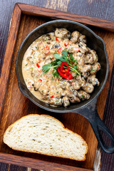 Fried snails in cream sauce, in a cast iron pan. On a wooden stand.