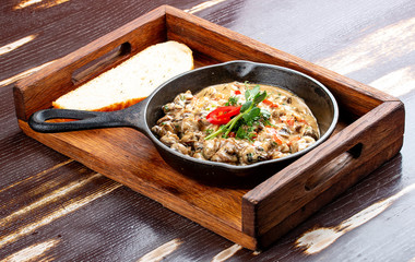 Fried snails in cream sauce, in a cast iron pan. On a wooden stand.