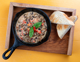 Fried snails in cream sauce, in a cast iron pan. On a wooden stand.