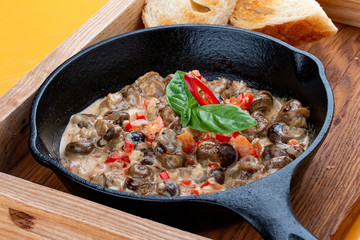 Fried snails in cream sauce, in a cast iron pan. On a wooden stand.