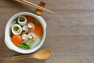 top view of seafood clear soup in a ceramic bowl on wooden table. asian homemade style food concept
