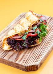 Bubble waffle sandwich with ham, tomato and lettuce. On a wooden board.