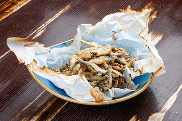Fried sprat in parchment on wooden background