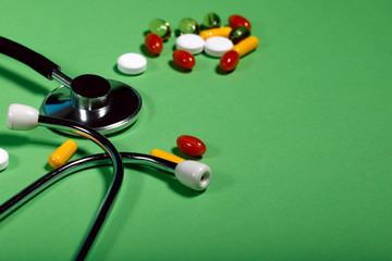 A group of bright medicine pills and a phonendoscope on a green background. Cropped shot, horizontal, side view. The concept of medicine and health. Crisis opioid painkiller and drug addiction concept