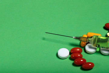 A group of bright medicine pills and a syringe on a green background. Cropped shot, horizontal, side view. The concept of medicine and health. Crisis opioid painkiller and drug addiction concept.