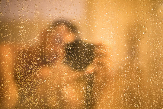 Fotograf hinter Regentropfen an einer Fensterscheibe bei gemütlichem Licht