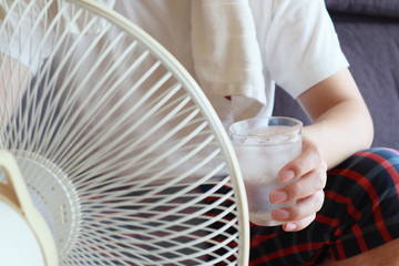 扇風機の風に当たりながら冷たい水を飲む男性