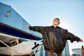 happy smiling kid in aviator glasses and large pilot jacket playing in front of white light private...