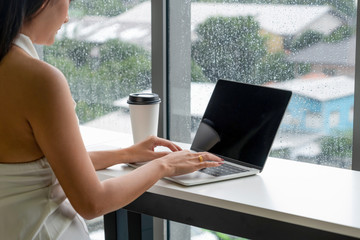 Young business woman using laptop computer while sitting at cafe table next to office windows.