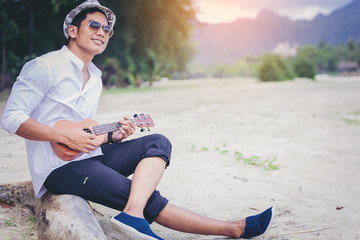 Young man with a white shirt playing a ukulele on a tropical beach. Travel and vacations concept..