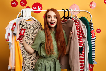 ginger stylish positive girl choosing clothes in the mall. close up photo. isolated yellow background. studio shot. lifestyle, hobby, free time, spare time