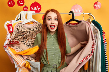 lovely ginger woman in stylish cothes standing among clothes which are on sale. close up photo....