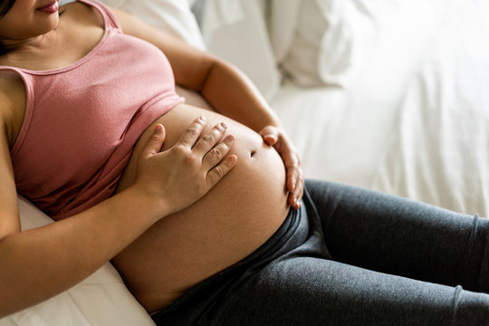 Pregnant woman feeling happy at home while taking care of her child. The young expecting mother holding baby in pregnant belly. Maternity prenatal care and woman pregnancy concept.
