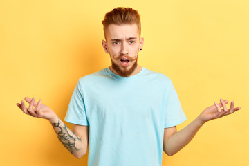 close up portrait of a young man with earring dressed casually showing ignorance on yellow background. isolated yellow background. studio shot.surprise concept . feeling and emotion