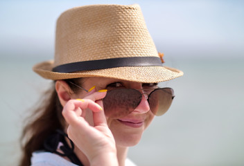Portrait of pretty girl in sunglasses and hat, holding glasses with hand, looks into camera, close-up