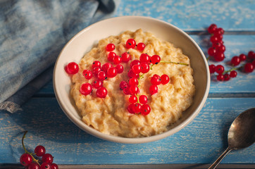 Breakfast of milk oatmeal with red currants on a blue wooden tray, spoon and denim napkin, as well as sprigs of currant, taken from close range