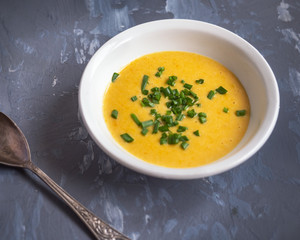 Soup of mashed potatoes with vegetables and cheese sprinkled with green onions, a tablespoon on a gray background