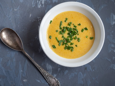 Soup of mashed potatoes with vegetables and cheese sprinkled with green onions, a tablespoon on a gray background