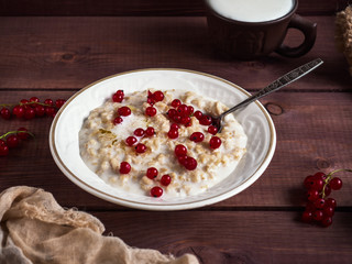 Breakfast of oatmeal porridge and fresh currant berries on a wooden tray, cotton thin napkin near the plate