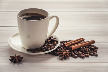a cup of coffee on a white wooden surface with cinnamon sticks