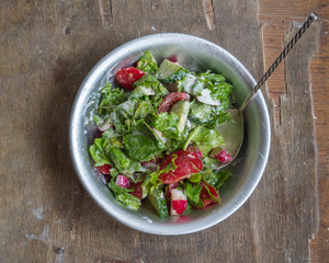 Fresh summer salad of tomatoes, cucumbers and aromatic herbs in a deep bowl, dressed with sour cream on an old wooden table