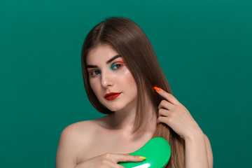 Portrait of beautiful young woman with bright color make-up combing hair with a green brush